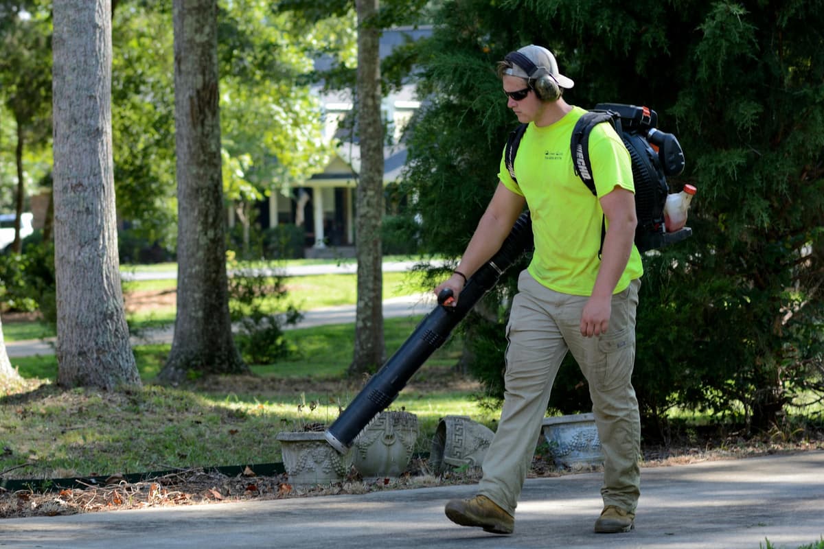 Lawn care worker clearing a residential driveway with a backpack blower